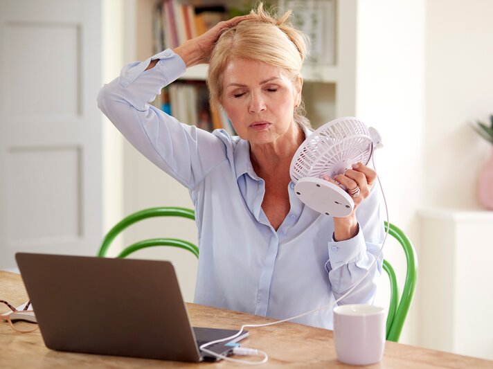 Ältere Dame ist heiß und sie hat einen kleinen Ventilator in der Hand und nimmt ihre Haare hoch | © adobe.stock.com/Monkey Business 