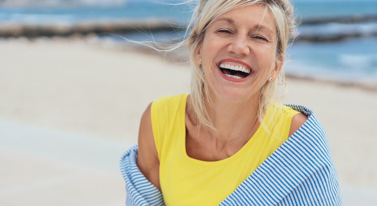 Dame mittleren Alters steht lachend am Strand