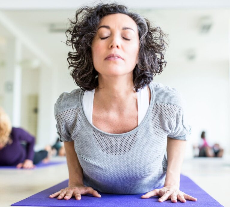 Frau übt in einem Yoga-Studio die Yoga-Übung Kobra aus. | © iStock/alvarez