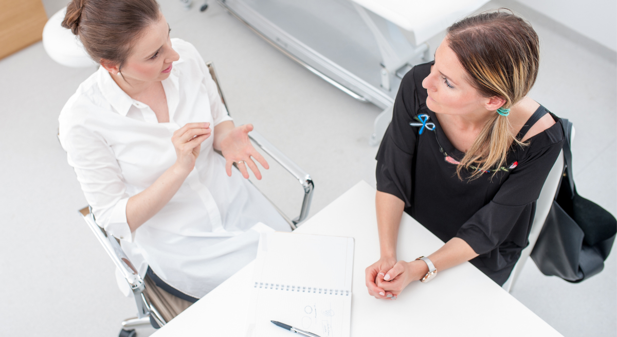 Ärztin im Gespräch mit einer Patientin, beide sitzen an einem Tisch, Perspektive von oben.