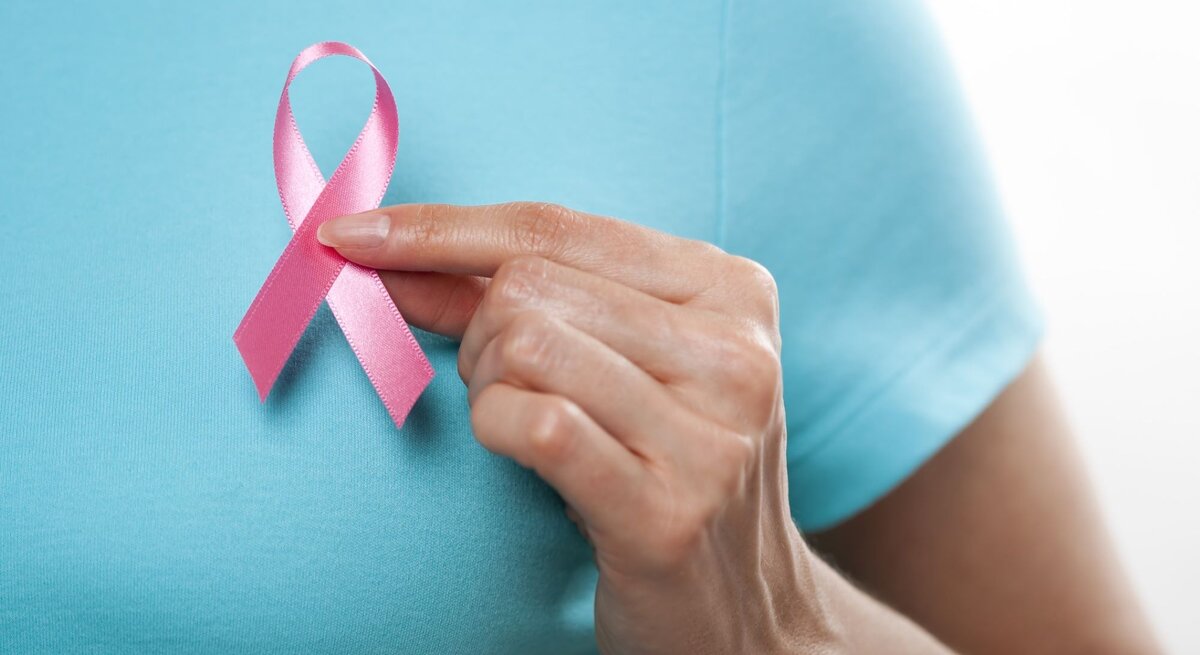 Eine Frau in einem blauen T-Shirt hält eine rosa Schleife vor die linke Brust.