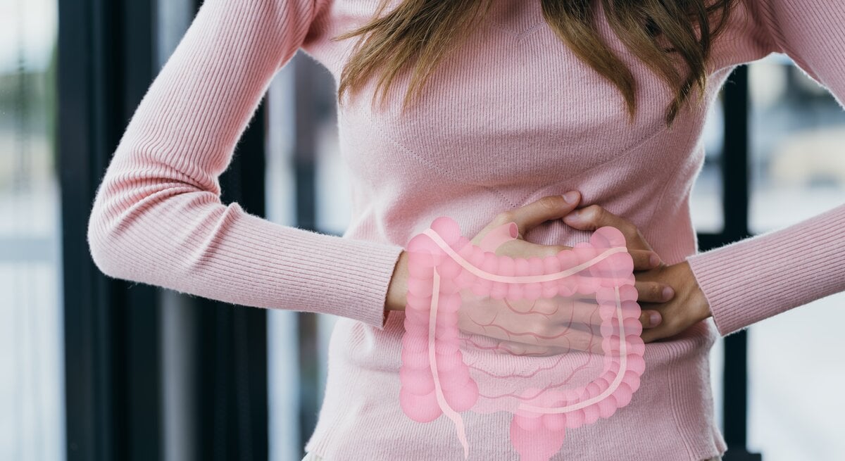 Auf dem Bild ist der mittlere Teil einer stehenden Person zu sehen, die ein rosafarbenes Oberteil trägt. Über den Bereich ihres Unterleibs ist eine transparente Grafik eines menschlichen Verdauungstrakts gelegt. Die Hände der Person sind auf Höhe des Magens positioniert, eine umfasst den Unterbauch, die andere unterstützt die erste Hand von der Seite. Das Bild hat einen erzieherischen Charakter und könnte verwendet werden, um auf die Bedeutung der Darmgesundheit hinzuweisen oder im Kontext der Darmkrebsvorsorge Aufmerksamkeit zu erregen. 