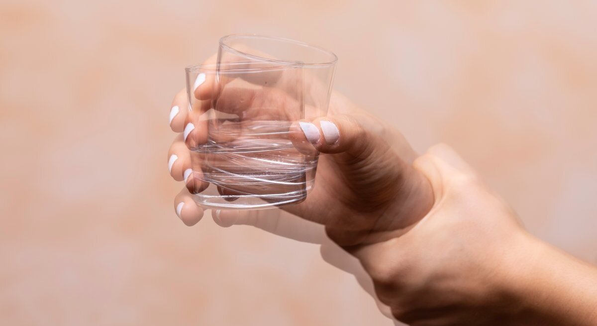 Ein Bild einer menschlichen Hand, die ein leeres Glas mit einer schnellen Bewegung schüttelt, wodurch eine Bewegungsunschärfe entsteht. Die Hautfarbe der Hand ist hell und der Hintergrund ist einfarbig und neutral, was den Fokus auf die Aktion der Hand legt. Der Zustand des Glases und die schnelle Bewegung könnten symbolisch für die Unsicherheit oder Fragilität des menschlichen Zustands stehen.
