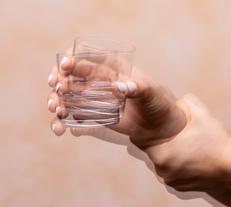 Ein Bild einer menschlichen Hand, die ein leeres Glas mit einer schnellen Bewegung schüttelt, wodurch eine Bewegungsunschärfe entsteht. Die Hautfarbe der Hand ist hell und der Hintergrund ist einfarbig und neutral, was den Fokus auf die Aktion der Hand legt. Der Zustand des Glases und die schnelle Bewegung könnten symbolisch für die Unsicherheit oder Fragilität des menschlichen Zustands stehen. | © shutterstock/sruilk