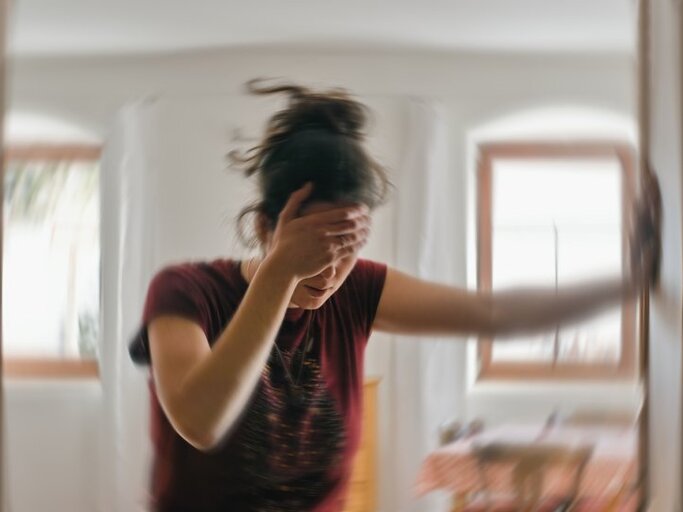 Frau hält sich die Stirn, während sich alles um sie herum dreht. | © Tunatura – stock.adobe.com
