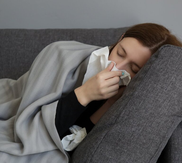 Frau liegt auf der Couch und schnäubt sich die Nase. | © Shutterstock/ triocean