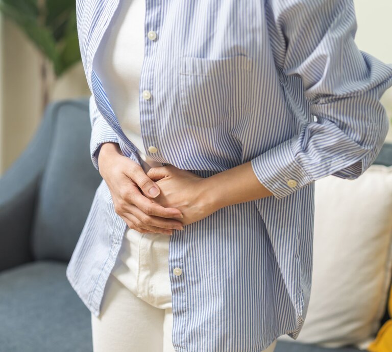 Junge Frau schaut zu ihrem aufgeblähtem Bauch und fasst diesen an. | © Shutterstock/Kmpzzz