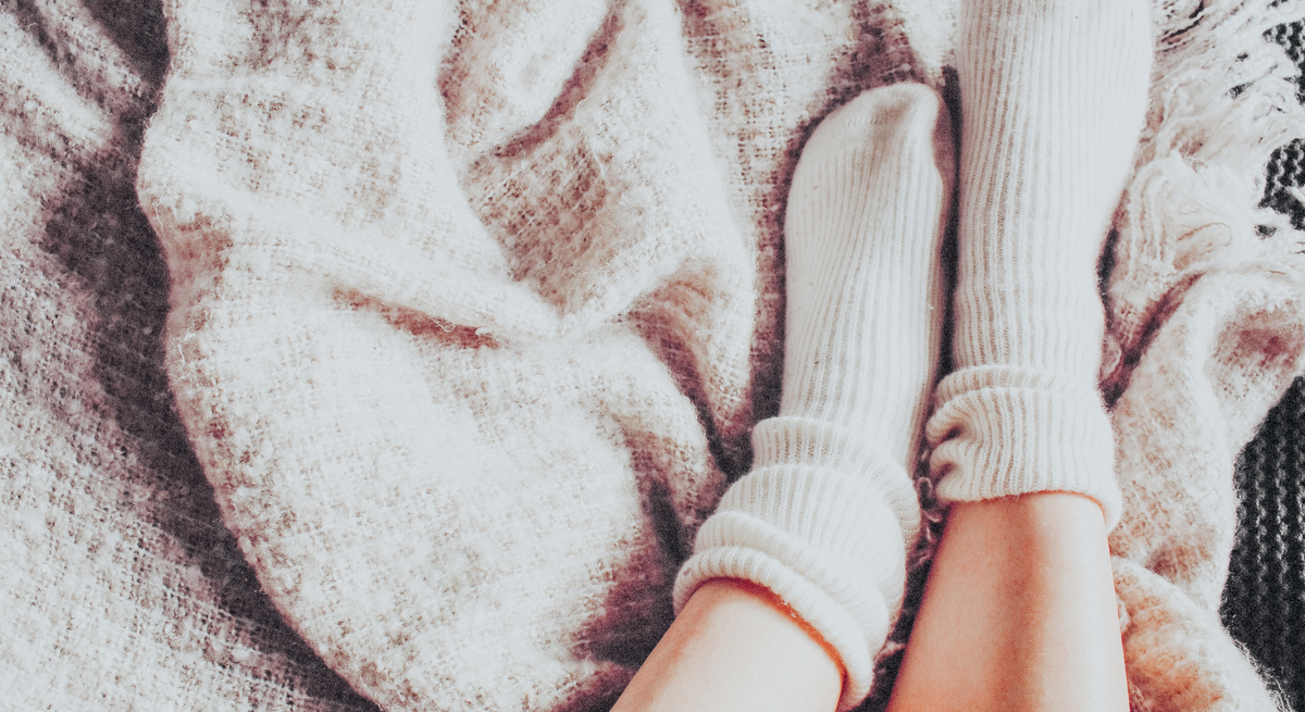 Zwei gepflegte Füße in kuscheligen Wollsocken stehen auf bunt gefärbtem Herbstlaub.