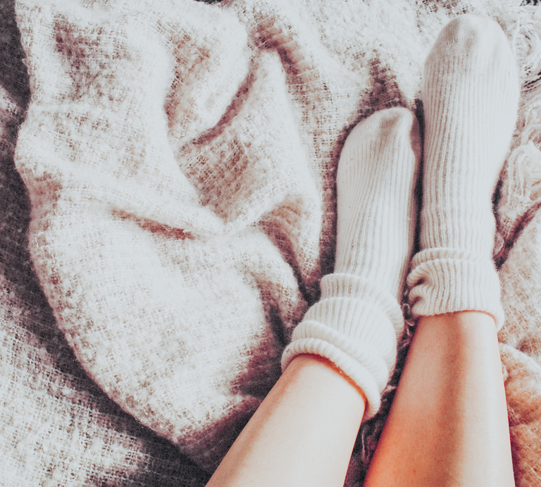 Zwei gepflegte Füße in kuscheligen Wollsocken stehen auf bunt gefärbtem Herbstlaub. | © Canva