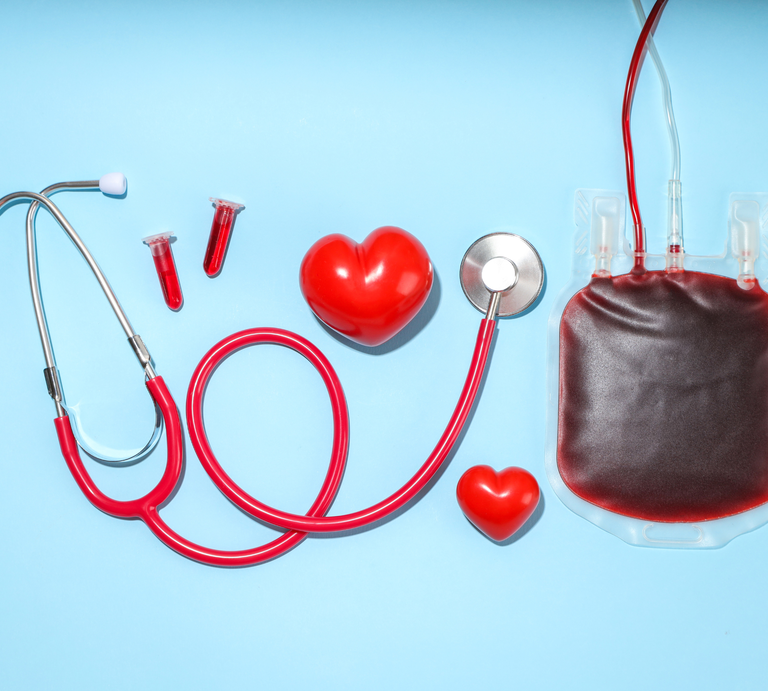 Medizinisches Stethoskop, ein Blutbeutel, zwei Blutprobenröhrchen und zwei rote Herzmodelle auf blauem Hintergrund arrangiert. | © Canva