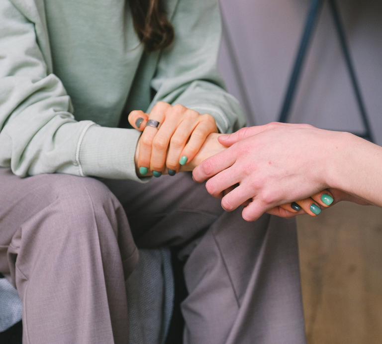 Auf einem Sofa halten sich zwei Menschen wortlos an den Händen, die Stimmung wirkt ruhig und einfühlsam. | © Canva