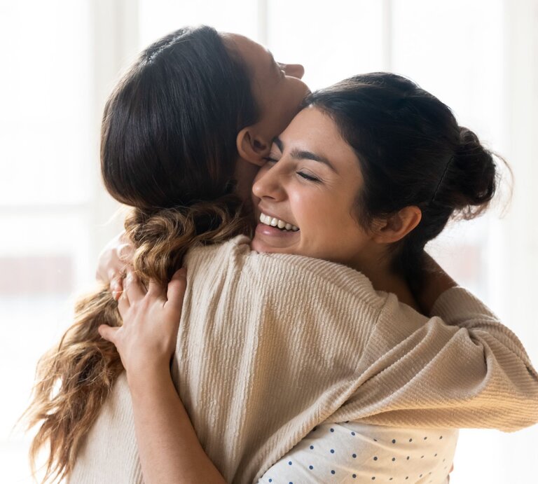 Zwei Frauen umarmen sich innig und lächeln dabei | © Shutterstock / fizkes