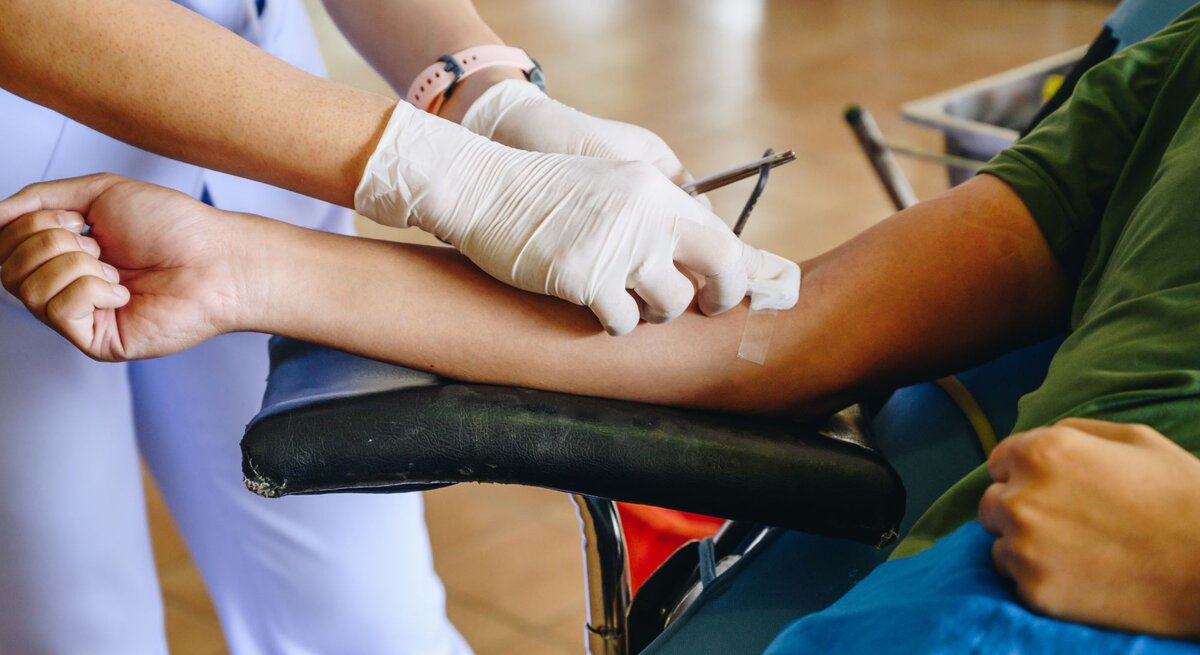 Es sind zwei Personen zu sehen. Eine Person liegt und spendet Blut, die andere setzt den Zugang.