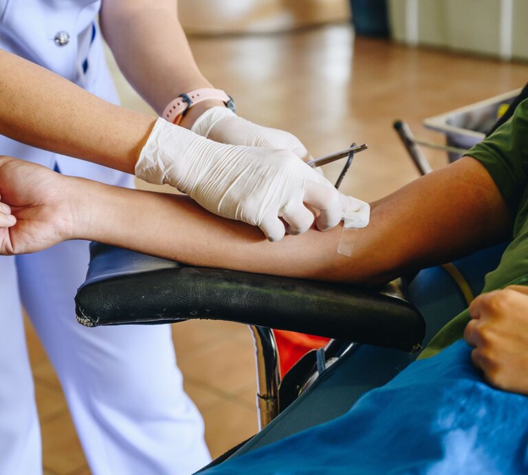 Es sind zwei Personen zu sehen. Eine Person liegt und spendet Blut, die andere setzt den Zugang. | © gettyimages/	Boy_Anupong