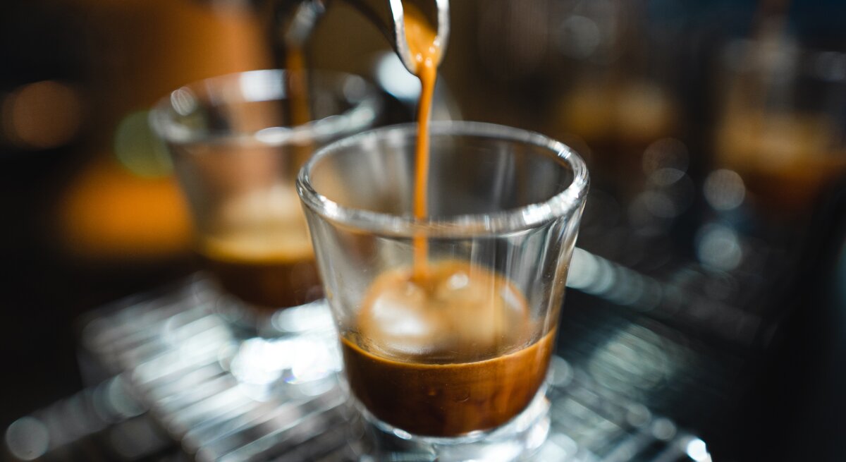 Frischer Espresso strömt geschmeidig aus einem Siebträger in ein transparentes Glas auf einem Metallgitter.