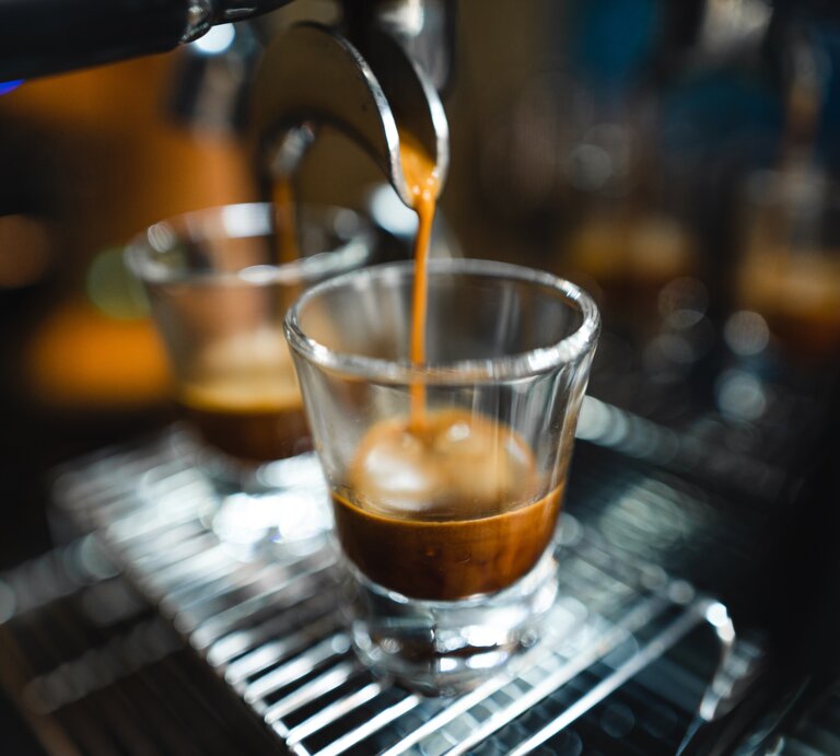 Frischer Espresso strömt geschmeidig aus einem Siebträger in ein transparentes Glas auf einem Metallgitter. | © Adobe Stock/ artrachen