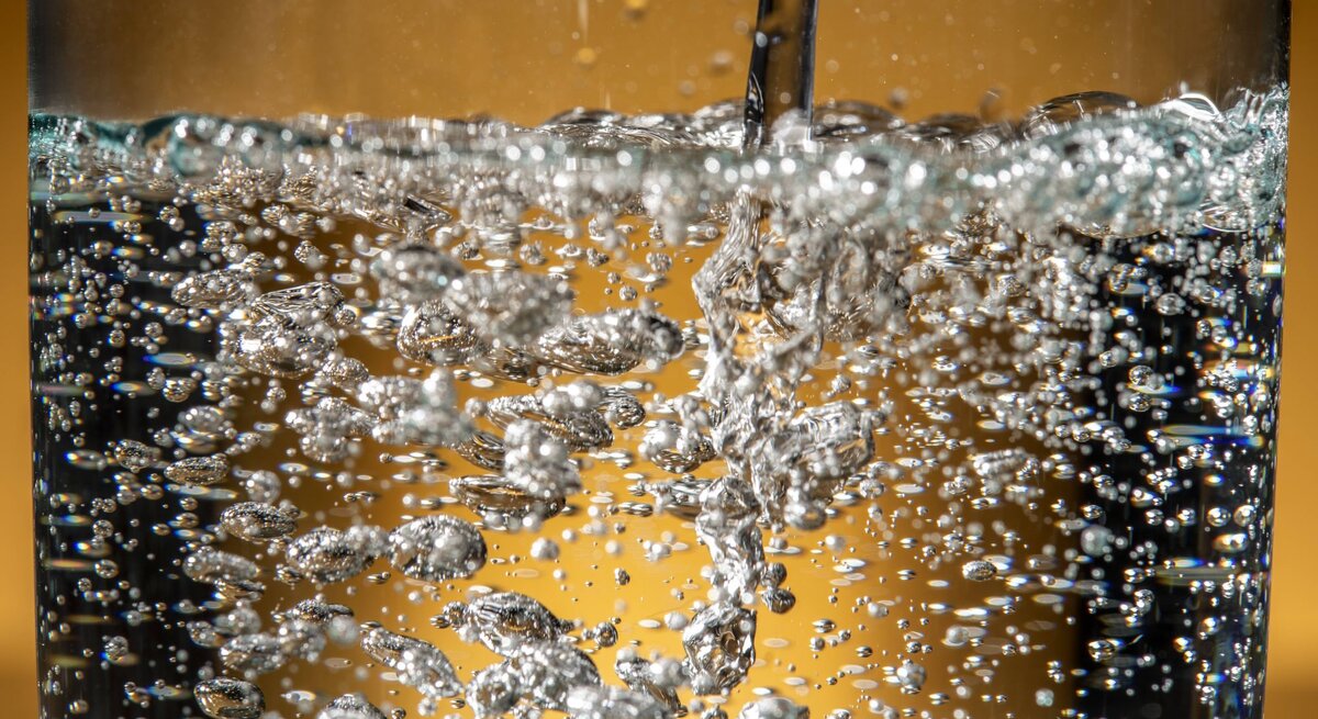 Wasser mit Kohlensäure wird in ein Glas gegossen und sprudelt.