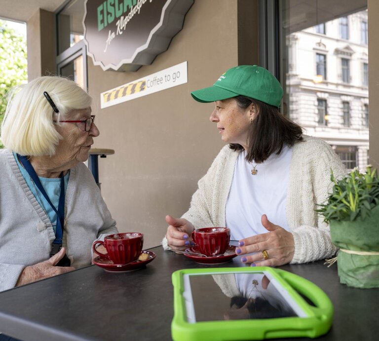 Preisträgerin Mitra Kassai mit einer Seniorin im Gespräch an einem Tisch | © Ulrike Schacht