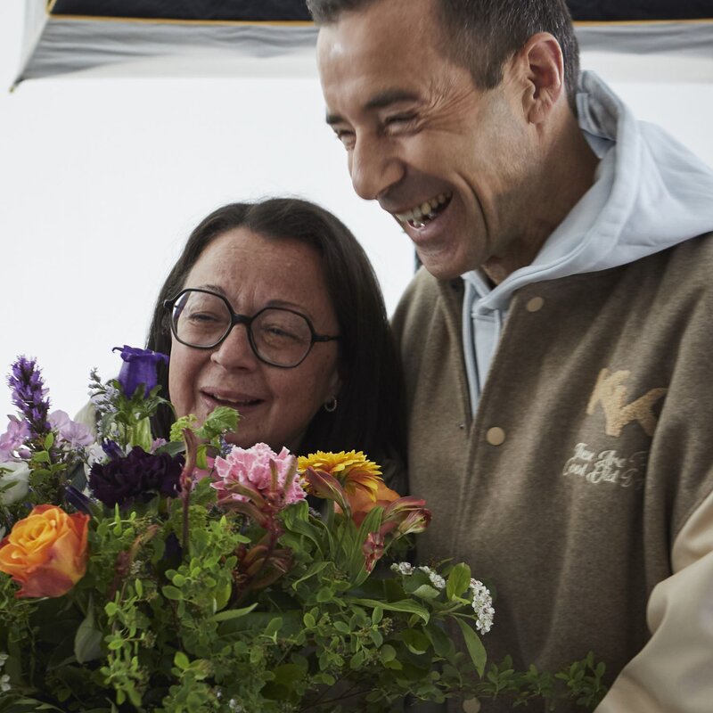 Eine ältere Frau mit Brille und ein lachender Mann in beiger Jacke halten gemeinsam einen bunten Blumenstrauß. | © dsphotos.de