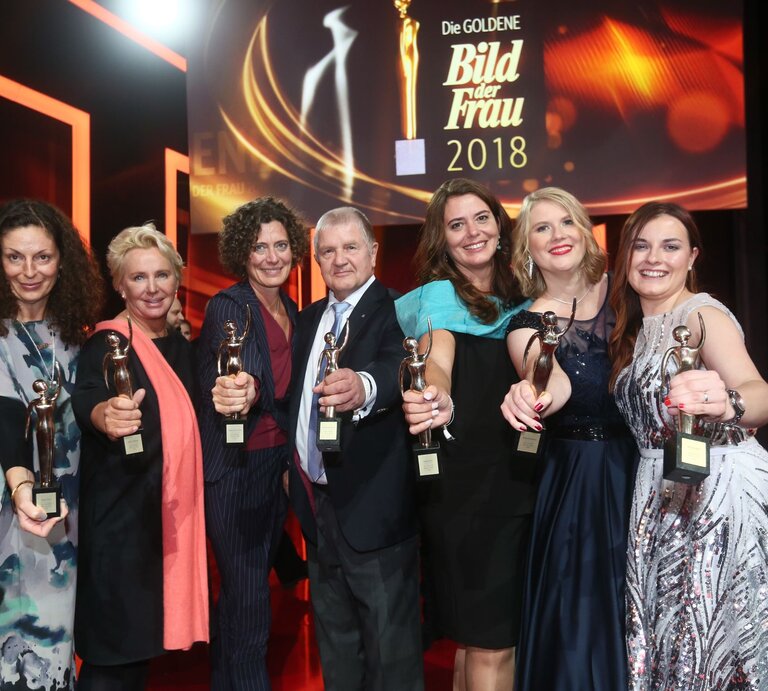 Sechs Preisträgerinnen in Abendkleidern und ein Mann der GOLDENEN BILD der FRAU-Gala 2018 halten ihre goldene Figurine in die Kamera  | © Guido Ohlenbostel