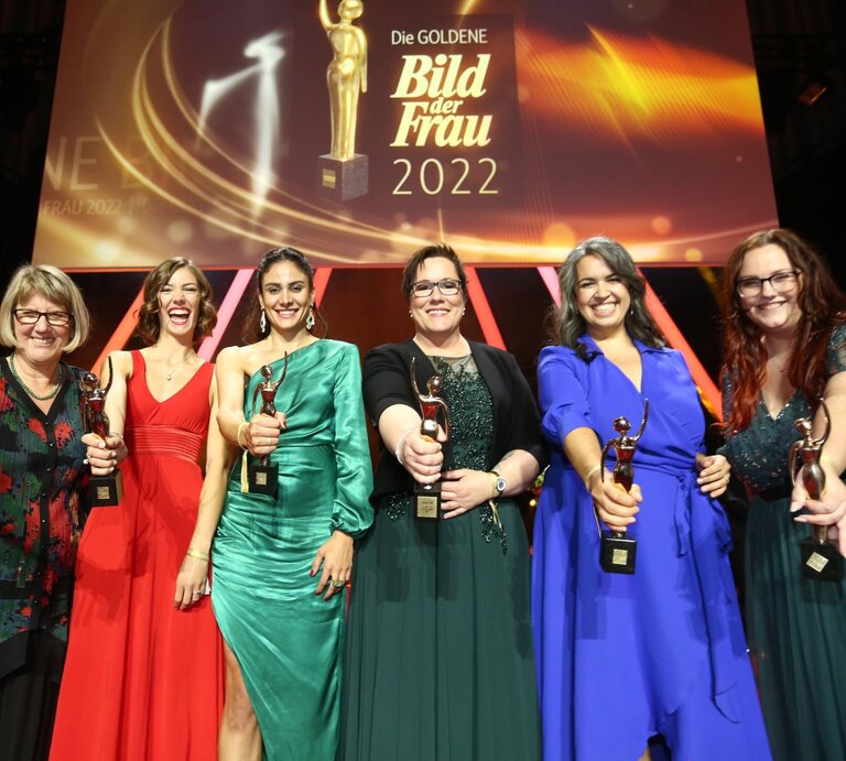 Sechs Preisträgerinnen in Abendkleidern auf der Bühne der GOLDENEN BILD der FRAU-Gala 2022 halten ihre goldene Figurine in die Kamera. | © Guido Ohlenbostel