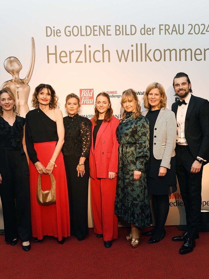 Sieben festlich gekleidete Personen lächeln auf einem roten Teppich vor einer Wand mit Schriftzug "Goldene Bild der Frau 2024 | © BILD der FRAU 