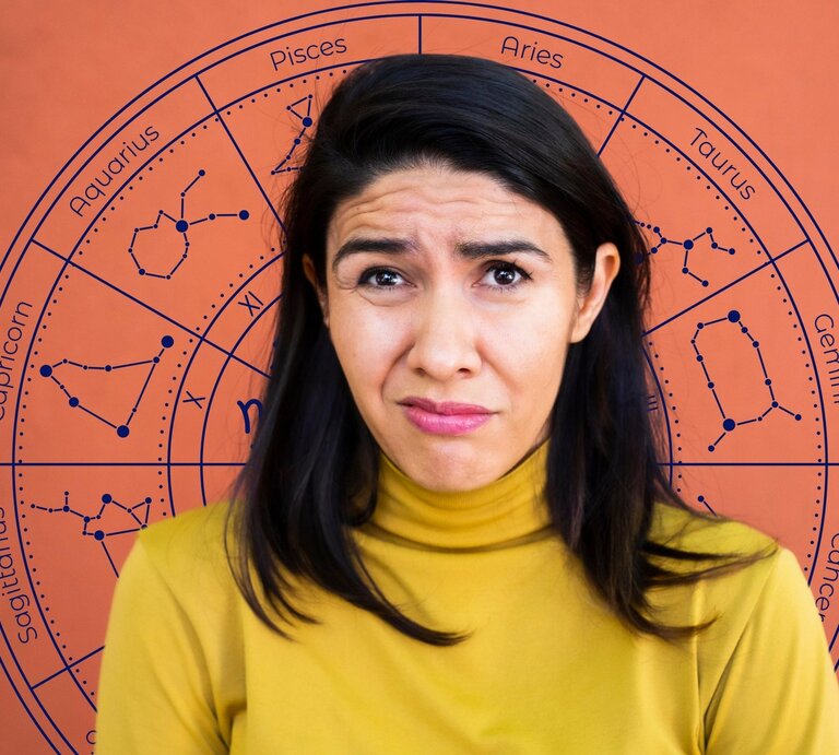 Eine Frau mit dunklen Haaren und gelbem Oberteil blickt besorgt und etwas ratlos in die Kamera. Hinter ihr ist ein großes Horoskop-Rad mit den zwölf Sternzeichen und ihren Sternbildern zu sehen. Symbolische Darstellung von Unsicherheit oder Pech im Zusammenhang mit Sternzeichen. | © Getty Images/ Sergio Mendoza Hochmann und WinWin.artlab via Canva.com [M]