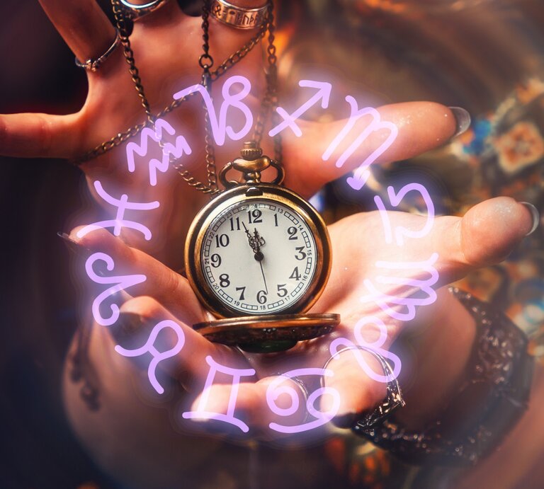 Eine Hand mit mehreren Ringen und einem Kettenarmband hält eine goldene Taschenuhr. Rund um die Uhr schweben leuchtende, violette Sternzeichen-Symbole in einem magischen Kreis. Der Hintergrund ist leicht verschwommen und zeigt bunte, gemusterte Stoffe, die eine mystische, spirituelle Atmosphäre schaffen. | © Getty Images/ Ildar Abulkhanov via Canva.com [M]
