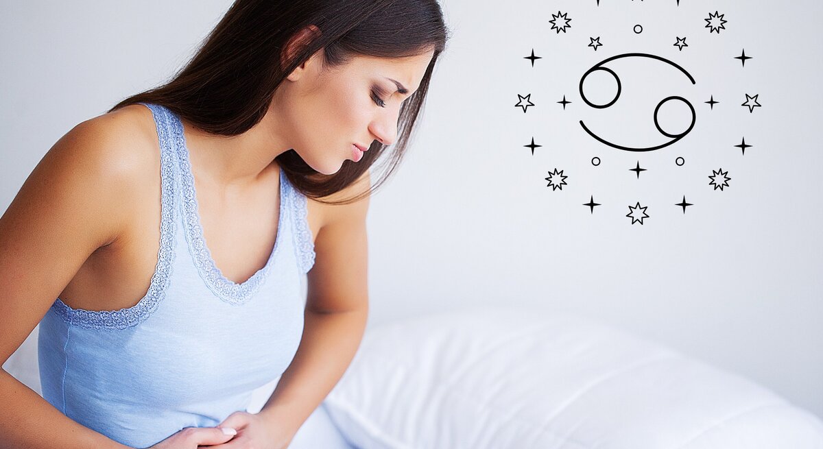 Das Bild zeigt eine junge Frau mit langen braunen Haaren, die ein hellblaues Oberteil trägt und sich vor Schmerzen den Bauch hält. Sie sitzt auf einem Bett mit einem weißen Kissen und einem weißen Bettlaken. Neben ihr ist das astrologische Symbol für Krebs, umgeben von kleinen Sternen, zu sehen. Die Frau wirkt angespannt und unwohl, was auf Bauchschmerzen oder Verdauungsprobleme hinweist. Das astrologische Symbol deutet darauf hin, dass das Bild in einem Zusammenhang mit einem Gesundheits-Horoskop für das Sternzeichen Krebs steht.