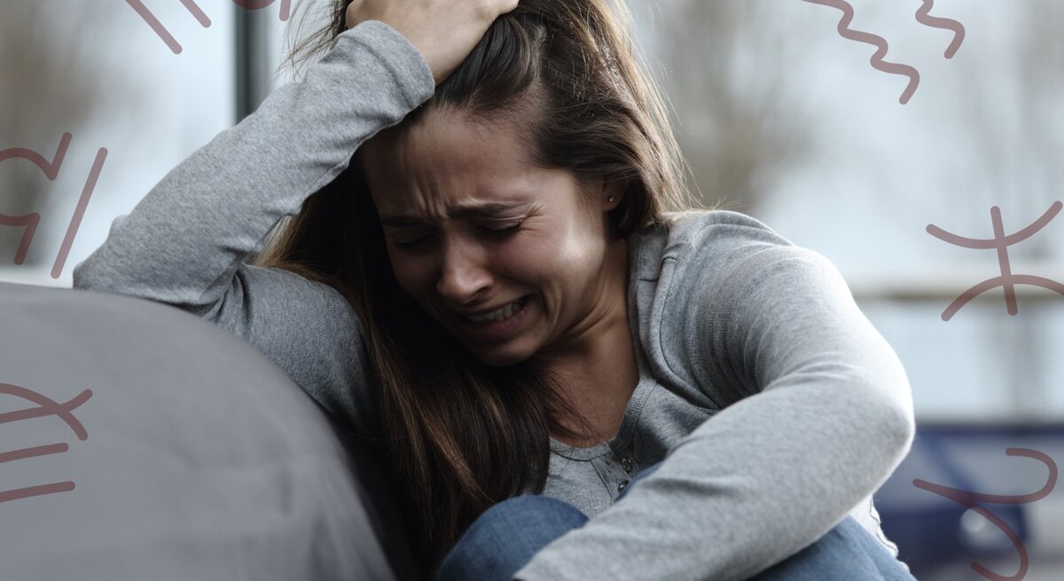 Eine junge Frau sitzt weinend und verzweifelt auf einem Sofa. Sie greift sich mit einer Hand in die Haare und wirkt sehr emotional und gestresst. Um sie herum sind verschiedene astrologische Symbole in einem dezenten Braunton zu sehen. Der Hintergrund ist unscharf und zeigt Bäume und ein Fenster, wodurch eine bedrückende Stimmung erzeugt wird.