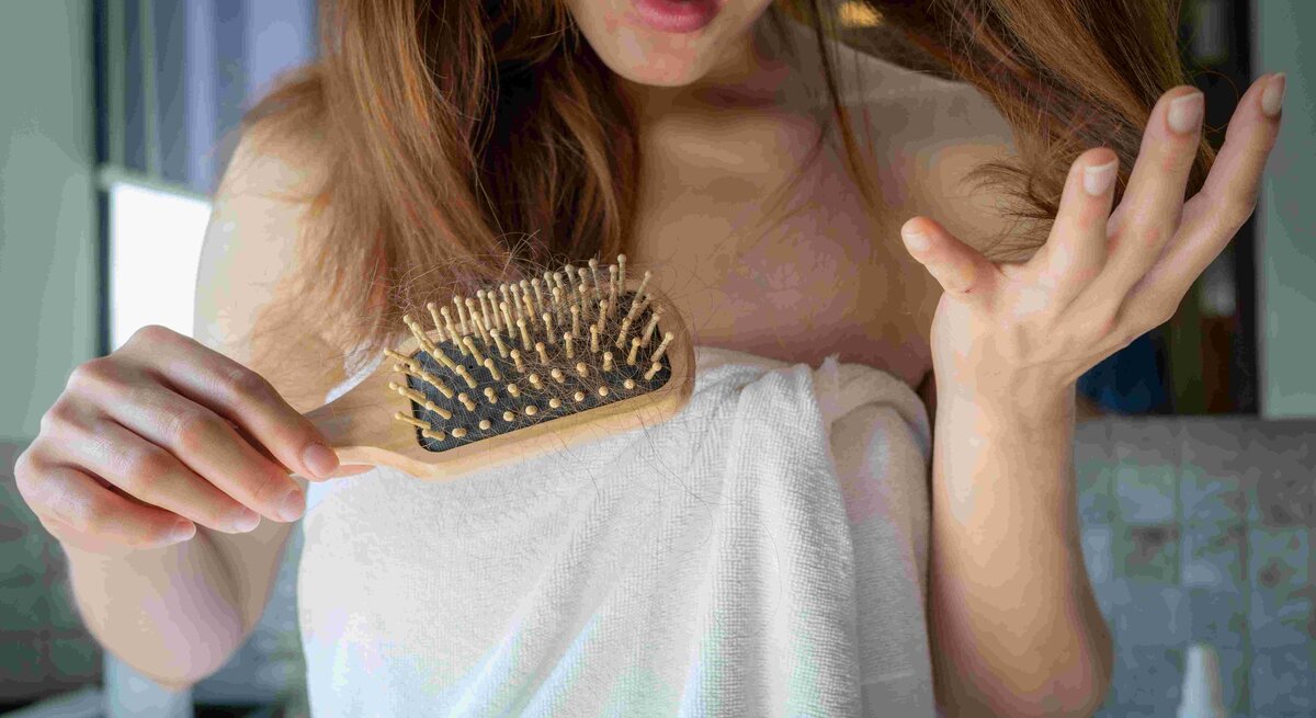 Nahaufnahme einer besorgten Frau, die einen Kamm hält und Haarausfall nach dem Bürsten ihrer Haare feststellt.