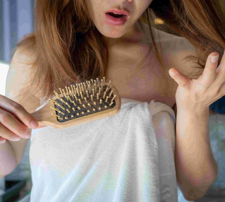 Nahaufnahme einer besorgten Frau, die einen Kamm hält und Haarausfall nach dem Bürsten ihrer Haare feststellt. | © Boy_Anupong via Gettyimages