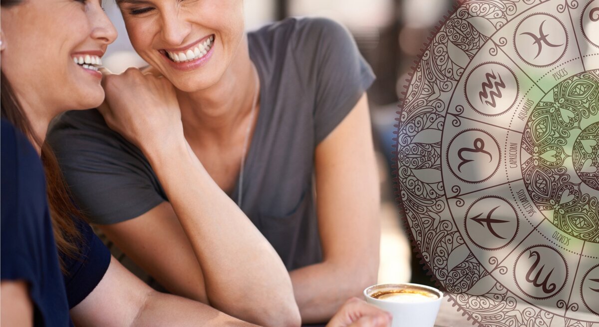 Ein fröhliches Bild zeigt zwei Frauen mittleren Alters, die lachend an einem Außentisch sitzen und Kaffee trinken. Die eine Frau mit braunem Haar flüstert der anderen, einer Frau mit blondem Haar, etwas ins Ohr, was beide zum Lachen bringt. Im Hintergrund ist ein halbtransparentes, großes Mandala mit astrologischen Symbolen zu sehen, was eine entspannte und freundliche Atmosphäre unterstreicht.