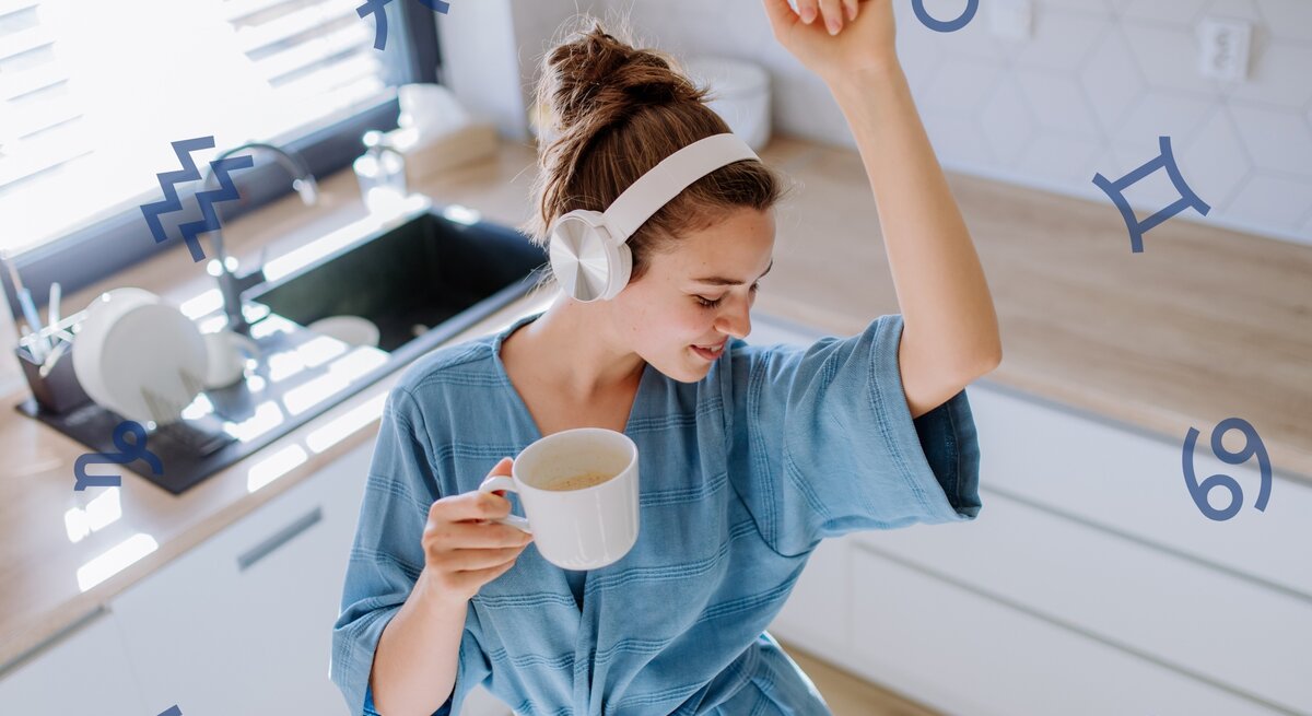 Eine junge Frau in einem entspannten blauen Kleid mit weißen Kopfhörern tanzt in einer hellen Küche und hält eine Tasse Kaffee. Sie scheint glücklich und energiegeladen zu sein. Über das Bild verteilt sind verschiedene Astrologie-Symbole wie Zwillinge, Wassermann, Steinbock und Krebs, die darauf hindeuten könnten, dass das Bild sich mit Astrologie oder Horoskopen beschäftigt.