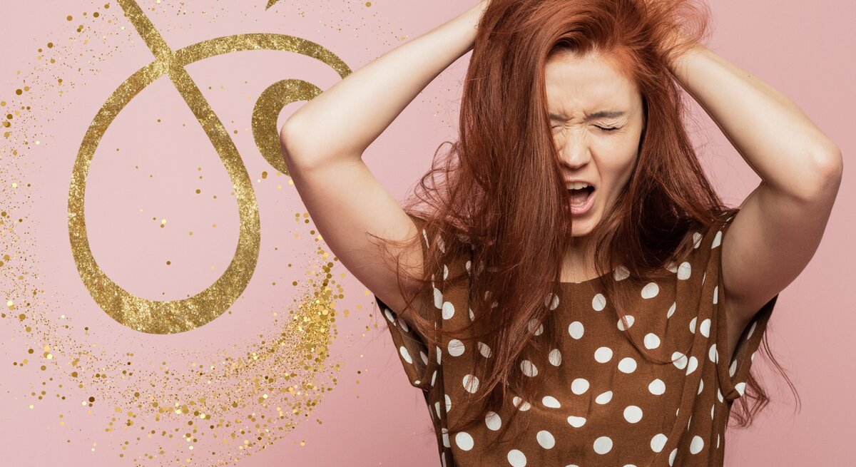 Ein Bild einer Frau mit auffälligem rotem Haar, die sichtlich frustriert und überfordert aussieht, während sie ihre Hände in ihr Haar krallt. Im Hintergrund ist das Symbol für das Sternzeichen Steinbock in Goldglitter zu sehen, welches auf einem rosa Hintergrund hervorsticht. Das Bild vermittelt eine Verbindung zwischen Astrologie und menschlichen Emotionen.