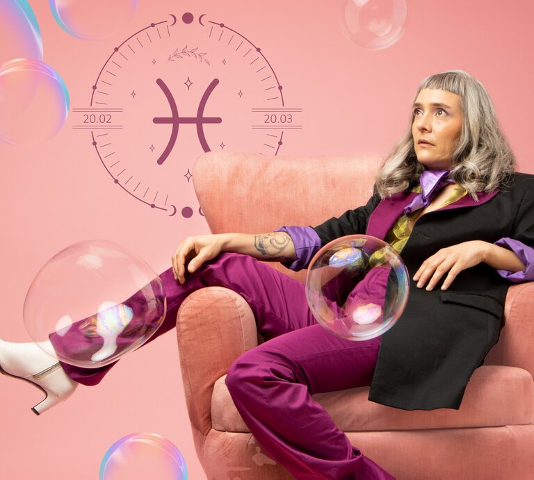 Eine Frau mit langen grauen Haaren trägt einen lila Retro-Anzug und sitzt in einem Sessel, das Bein lässig über die Lehne geschlagen. Sie ist umgeben von Seifenblasen und neben ihr ist das astrologische Symbol des Sternzeichens Fische in einem Kreis zu sehen. | © diversifylens/ Lina Vanessa Merchán Jimenez,  Keronyart's Images/ Be keronyart und Jaya Adi Prastya Design via Canva.com [M]
