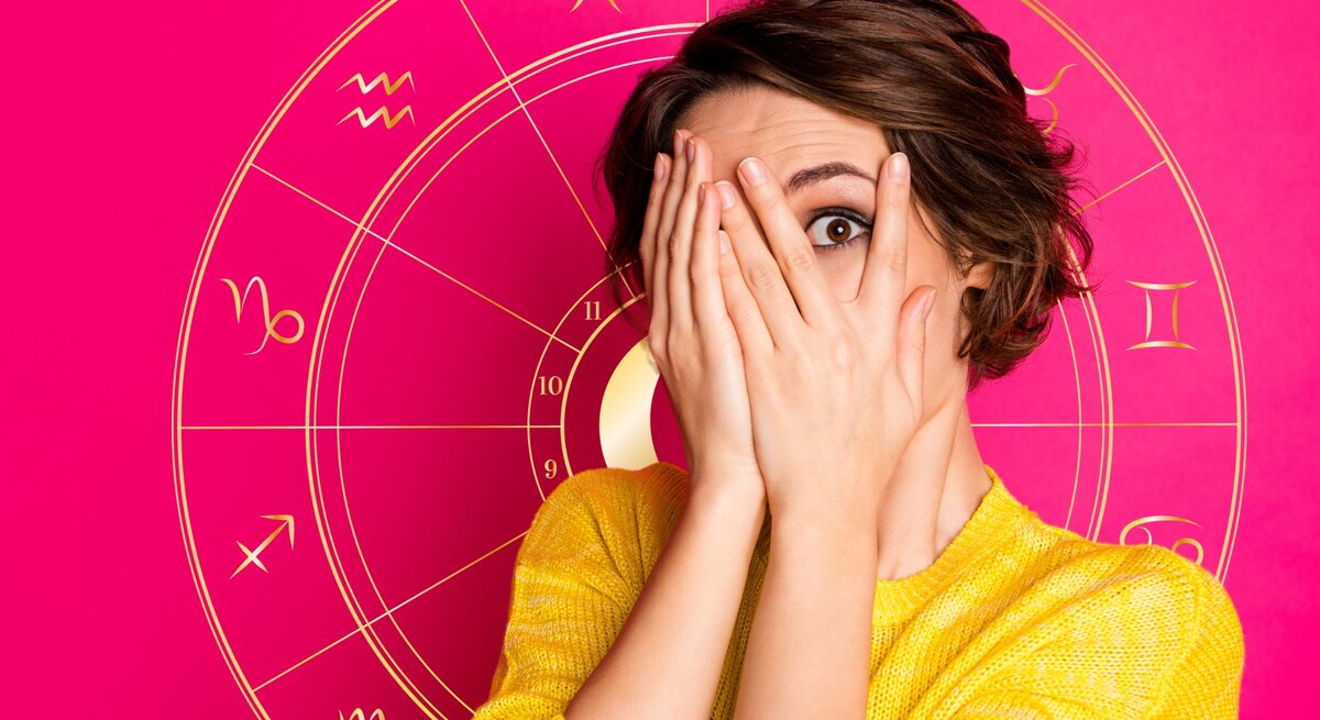 Eine überraschte Frau in einem gelben Oberteil hält ihre Hände vor ihr Gesicht und späht durch ihre Finger. Im Hintergrund ist eine leuchtend rosa Grafik mit astrologischen Symbolen, darunter das Rad des Tierkreises mit den Zeichen von Widder bis Fische.