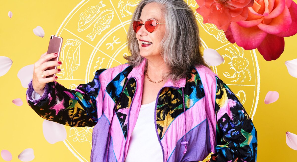Frau mit grauen Haaren die ein Handy hält und lächelt. Umgeben von Blumen und astrologischen Zeichen.