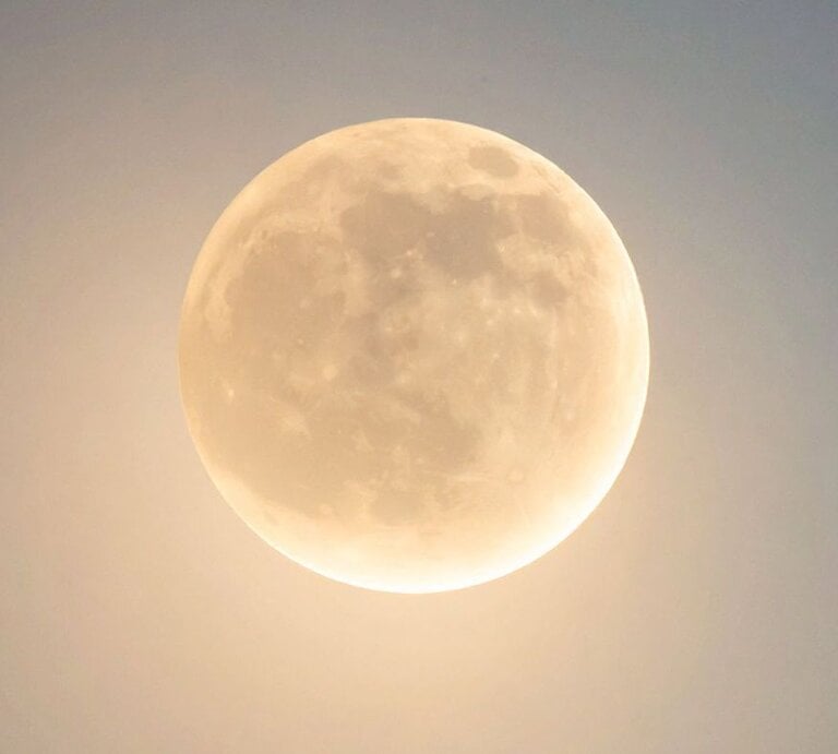 Ein Vollmond am Nachthimmel mit sanftem, goldenem Schimmer. Die Oberflächenstrukturen des Mondes, wie Krater und Ebenen, sind klar erkennbar. Der Himmel wirkt leicht aufgehellt und hat nur einen dezenten Blauton. | © TrueCreatives via Canva.com