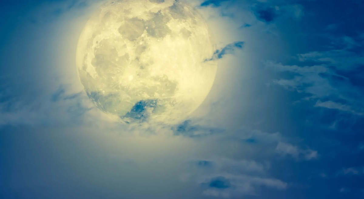 Mondhoroskop Oktober 2025: Heller Vollmond am Nachthimmel, umgeben von leicht ziehenden Wolken in Blau- und Weißtönen.