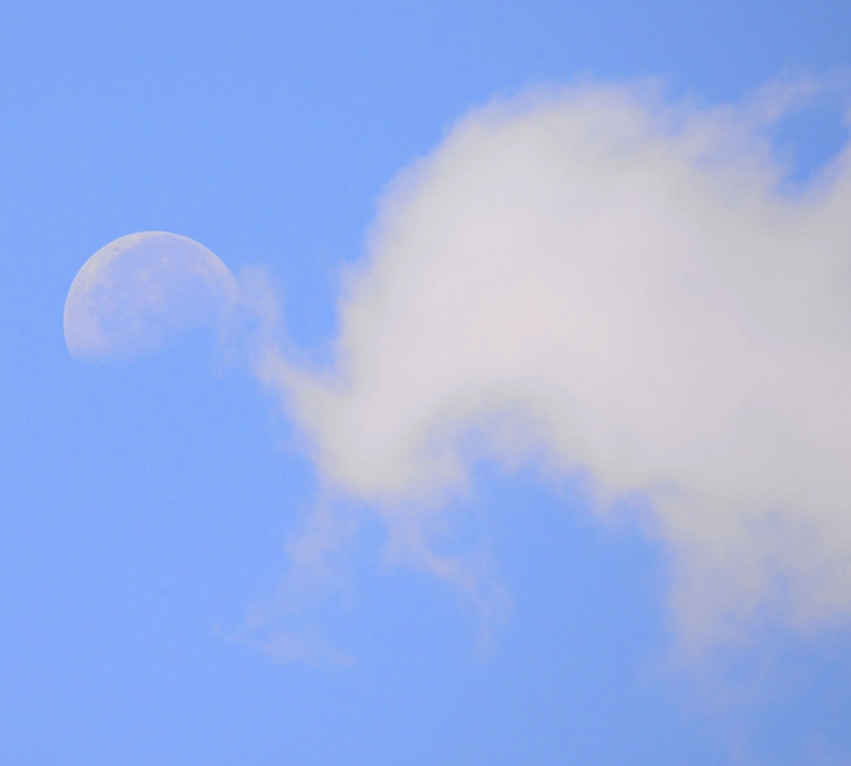 Halbmond am hellblauen Himmel, teilweise von einer weißen Wolke verdeckt. | © Getty Images/ ernesto-photos via Canva.com