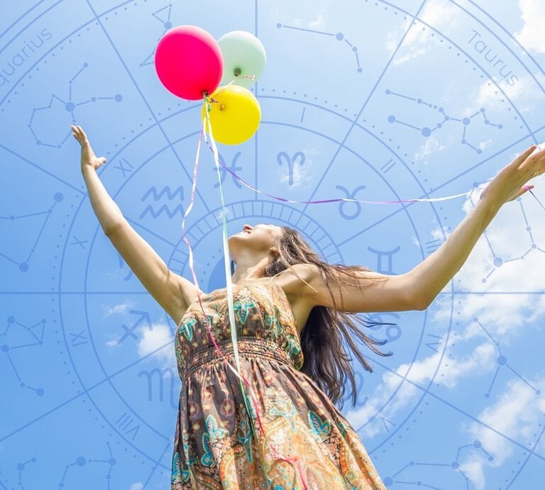 Frau in Sommerkleid hält bunte Luftballons in den Händen und blickt freudig in den Himmel, im Hintergrund ein transparenter Tierkreis mit Sternzeichen-Symbolen. | © Oneinchpunch und WinWin.artlab via Canva.com [M]