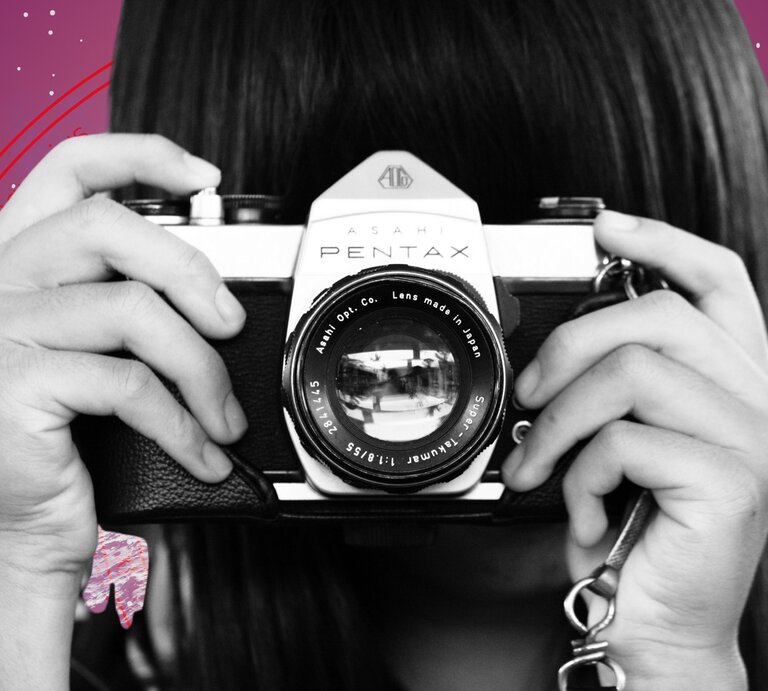 Eine Person hält eine analoge Kamera vom Typ Asahi Pentax vor das Gesicht, bereit zum Fotografieren. Im Hintergrund ist ein stilisiertes astrologisches Rad mit Sternzeichen auf violettem Grund zu sehen – Symbol für den Blick in die Zukunft und das Zusammenspiel von Kreativität und kosmischem Einfluss. | © Pexels/ Gabriel Peter, WinWin.artlab, sceptical cactus, OyoyStudio, kucingpink/ mohamad imron hamsyah und Jaya Adi Prastya via Canva.com [M]