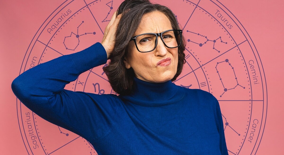 Eine Frau mittleren Alters mit Brille und dunklem Haar trägt einen blauen Rollkragenpullover und hat einen skeptischen, nachdenklichen Gesichtsausdruck. Sie kratzt sich am Kopf, als wäre sie unsicher oder verwirrt. Im Hintergrund befindet sich eine astrologische Tierkreisgrafik mit den Sternzeichen und ihren Symbolen auf einem rosa Hintergrund. Das Bild vermittelt eine humorvolle oder fragende Haltung gegenüber Horoskopen und Astrologie.