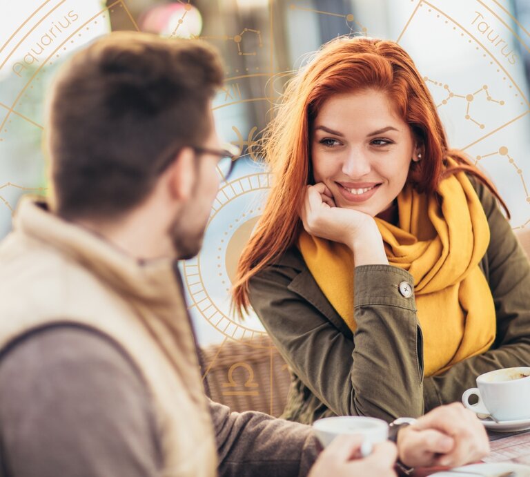 Ein junges Paar sitzt in einem Café und unterhält sich bei einer Tasse Kaffee. Die Frau mit roten Haaren und gelbem Schal lächelt ihren Gesprächspartner an, während sie ihren Kopf auf eine Hand stützt. Im Hintergrund ist ein astrologisches Rad mit den zwölf Tierkreiszeichen und Sternbildern eingeblendet, was eine Verbindung zwischen dem Gespräch und astrologischen Einflüssen andeutet. Die Szene wirkt warm und harmonisch. | © Getty Images/ Jovanmandic und Winwin.artlab via Canva.com [M] 