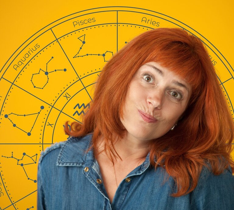 Frau mit roten Haaren in Jeanshemd steht vor einem gelben Hintergrund mit einem großen astrologischen Tierkreis. Die Sternzeichen und ihre Symbole sind kreisförmig um sie herum angeordnet. Die Frau schaut mit einem leicht schiefen Lächeln und fragendem Gesichtsausdruck in die Kamera. Das Bild vermittelt einen humorvollen, aber auch nachdenklichen Blick auf das Thema Horoskop und Pechsträhnen. | © Getty Images/ brusinski und WinWin.artlab via Canva.com [M]