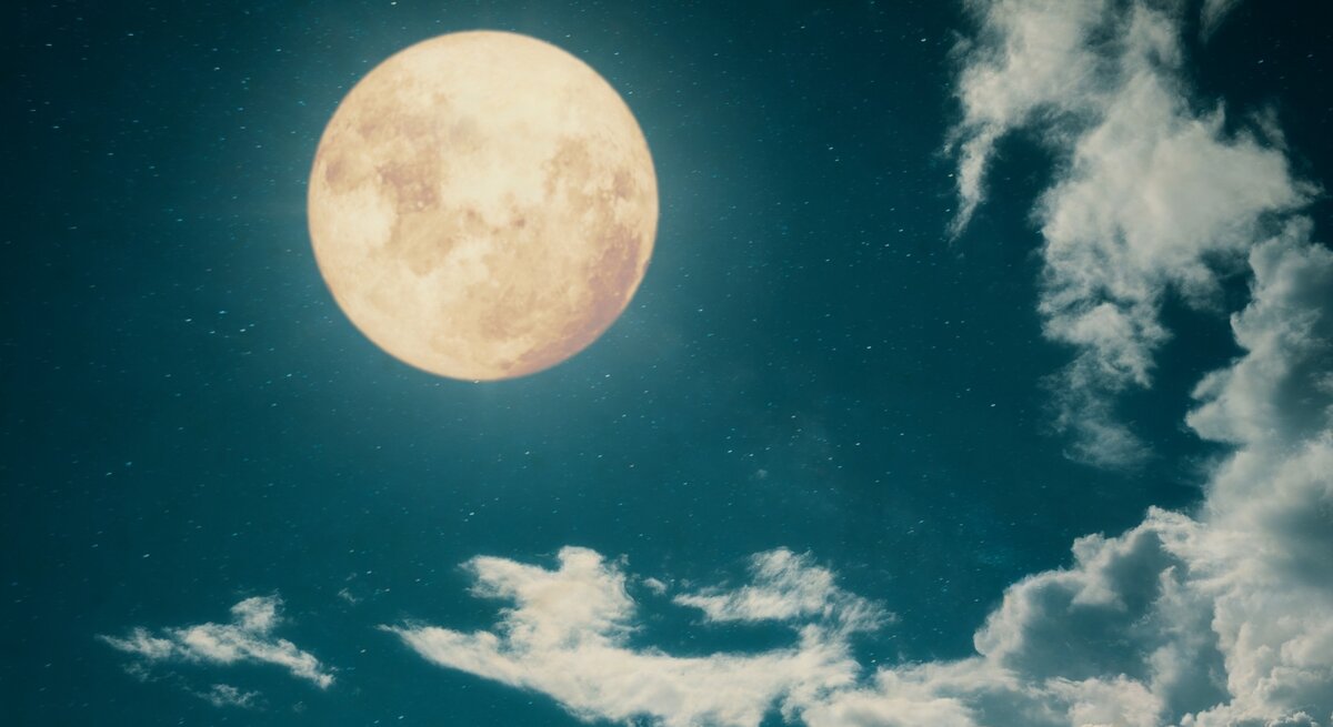 Ein großer, leuchtender Vollmond am Nachthimmel, umgeben von Sternen und sanften, weißen Wolken. Der Himmel ist tiefblau und erzeugt eine ruhige, mystische Atmosphäre.