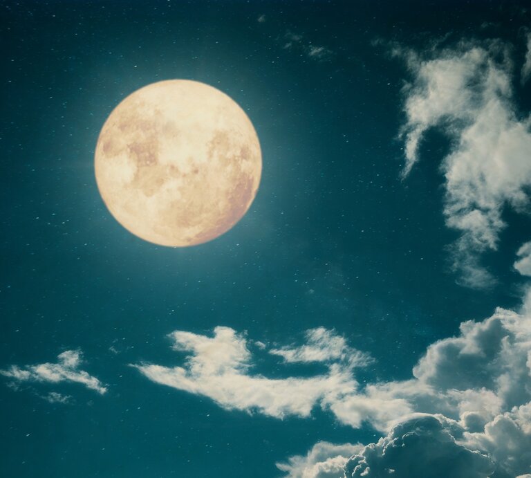 Ein großer, leuchtender Vollmond am Nachthimmel, umgeben von Sternen und sanften, weißen Wolken. Der Himmel ist tiefblau und erzeugt eine ruhige, mystische Atmosphäre. | © Getty Images/ jakkapan21 via Canva.com