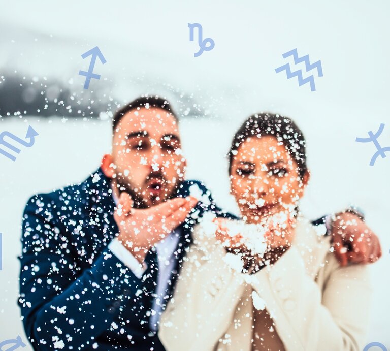 Ein fröhliches Paar in eleganter Winterkleidung steht in einer verschneiten Landschaft. Beide halten Schnee in ihren Händen und pusten ihn spielerisch in die Luft, wodurch Schneeflocken um sie herumwirbeln. Der Mann trägt einen dunkelblauen Anzug, die Frau einen cremefarbenen Mantel. Ihr Gesichtsausdruck strahlt Freude und Romantik aus. Im Hintergrund sind schneebedeckte Hügel und eine winterliche Landschaft zu erkennen. Um das Paar herum schweben verschiedene astrologische Symbole, darunter für Schütze, Skorpion, Wassermann und Fische, was eine Verbindung zur Astrologie und zu einem Flirthoroskop suggeriert. | © Getty Images/ Minet Zahirovic und Chikovnaya via Canva.com [M]