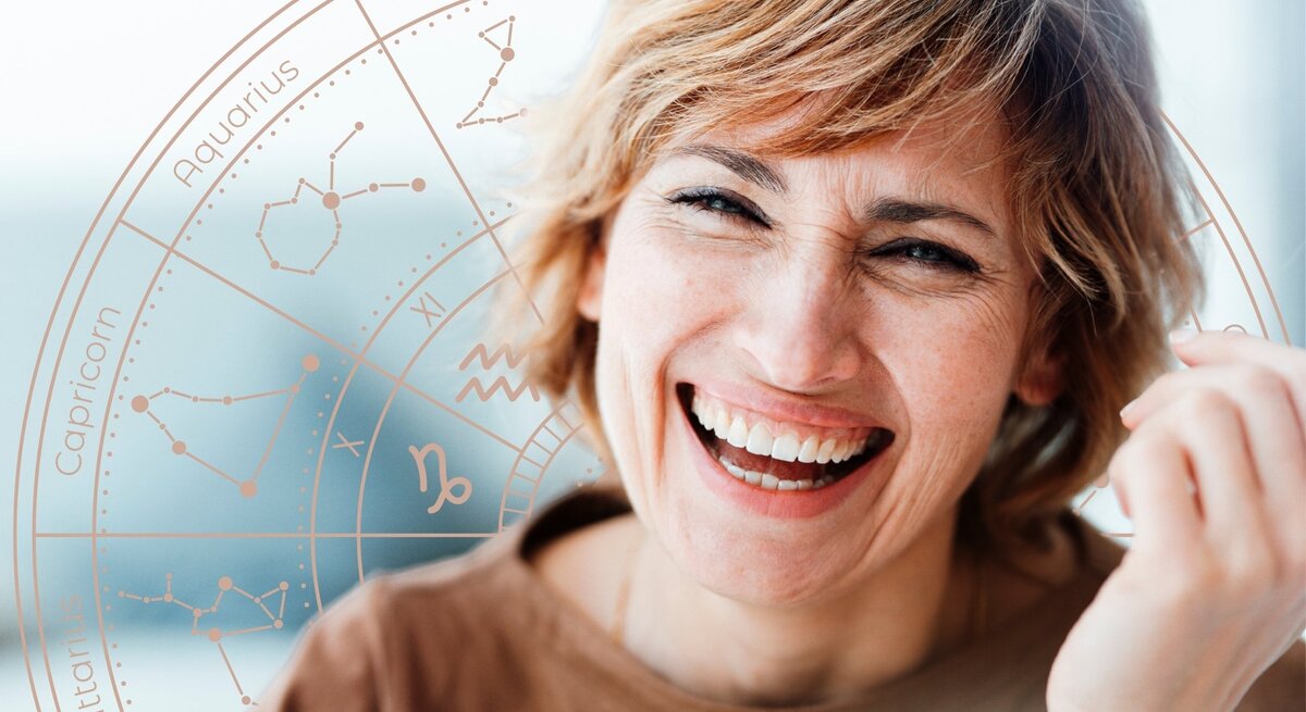 Fröhliche Frau mit kurzen, blonden Haaren lacht herzlich vor einem dezenten astrologischen Sternzeichen-Rad. Der Hintergrund ist hell und freundlich, das Rad mit den Tierkreiszeichen schimmert in sanften Pastelltönen. Das Bild strahlt Optimismus, Lebensfreude und eine positive astrologische Botschaft aus.